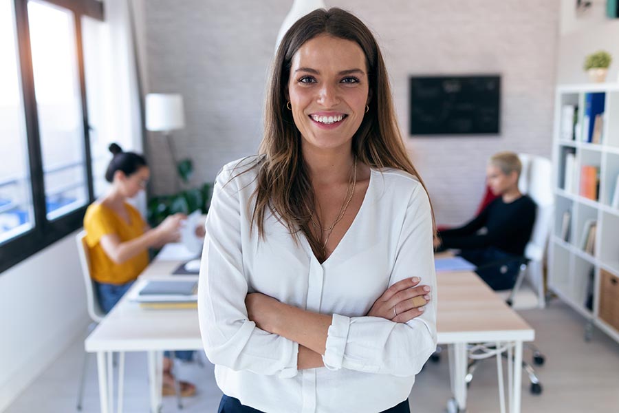 Business Insurance - Cheerful Businesswoman Stands With Arms Crossed in Front of Her Employees in a Modern Office